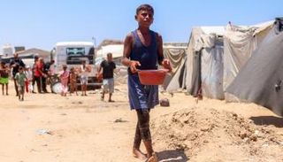صبي فلسطيني يحمل وعاءً ويسير بين خيام النازحين في غزة